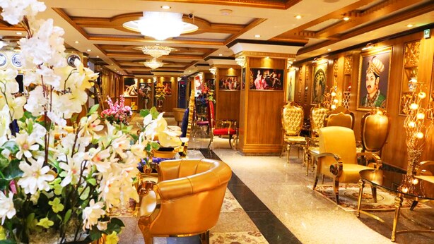 Un lobby de hotel lujoso con decoración elaborada, que incluye un mostrador de recepción dorado, asientos cómodos y un arreglo floral grande.