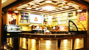 Zona de bar con mostrador, estantes de aperitivos, una pantalla grande y un letrero de neón.
