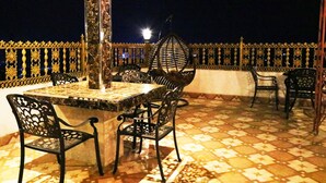 Un área de estar al aire libre con una mesa, sillas, una lámpara colgante decorativa y un suelo estampado.