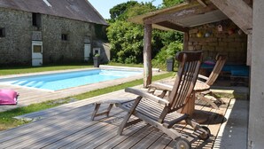 A wooden deck with a pool, lounge chairs, and a stone building in the background.