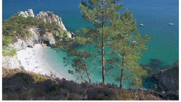 A coastal landscape with a beach, clear turquoise waters, and rocky outcrops.