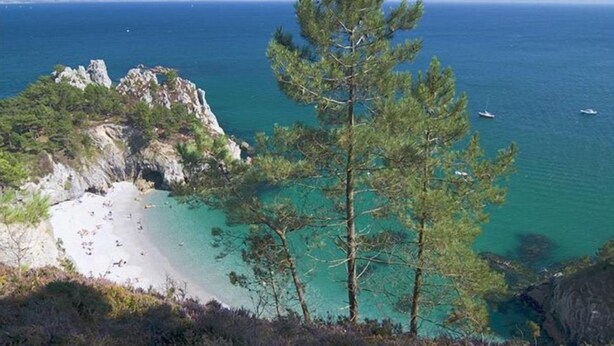 A coastal landscape with a beach, clear turquoise waters, and rocky outcrops.