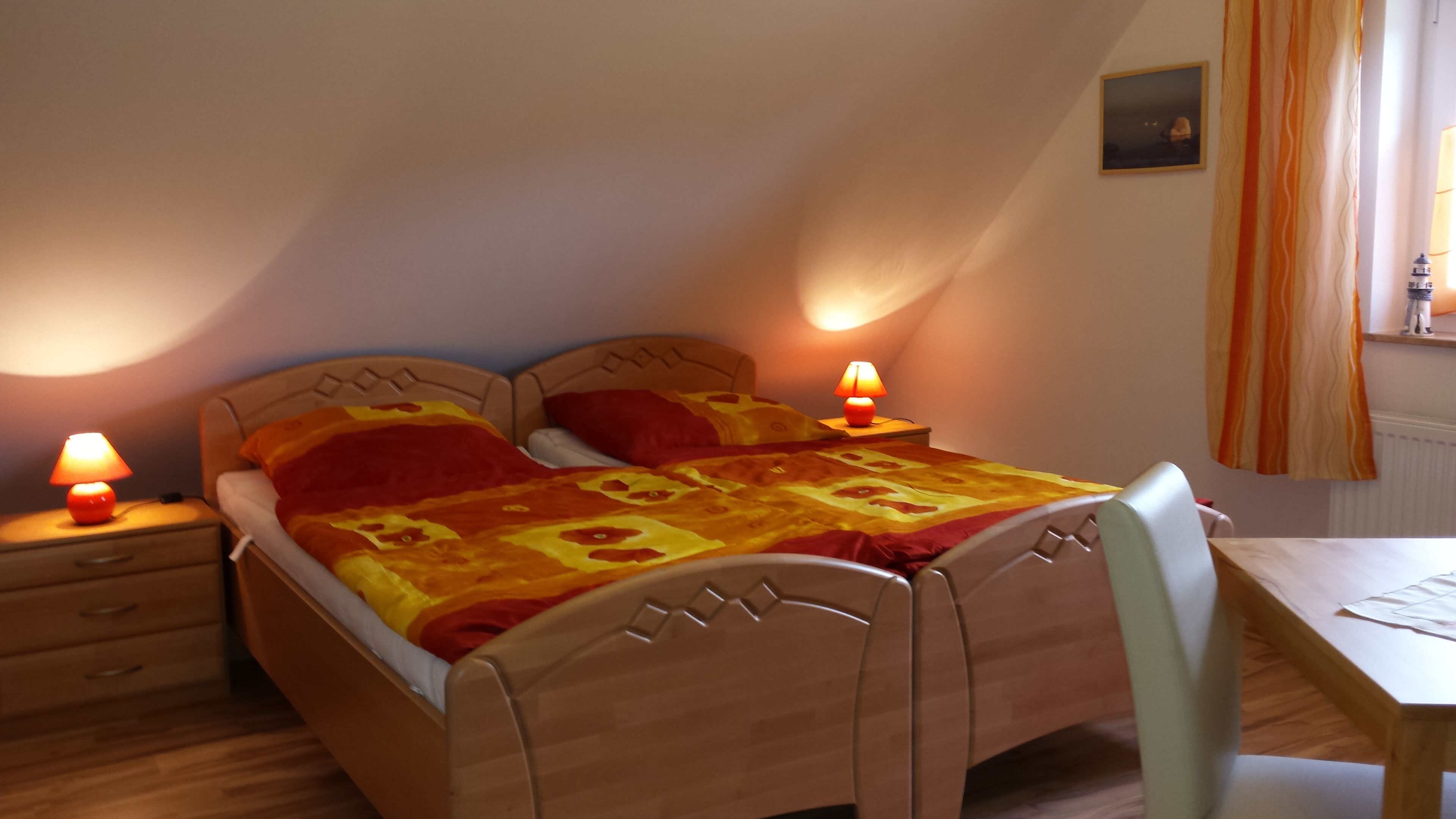A bedroom with a wooden bed, two bedside tables with lamps, a desk, and a chair.