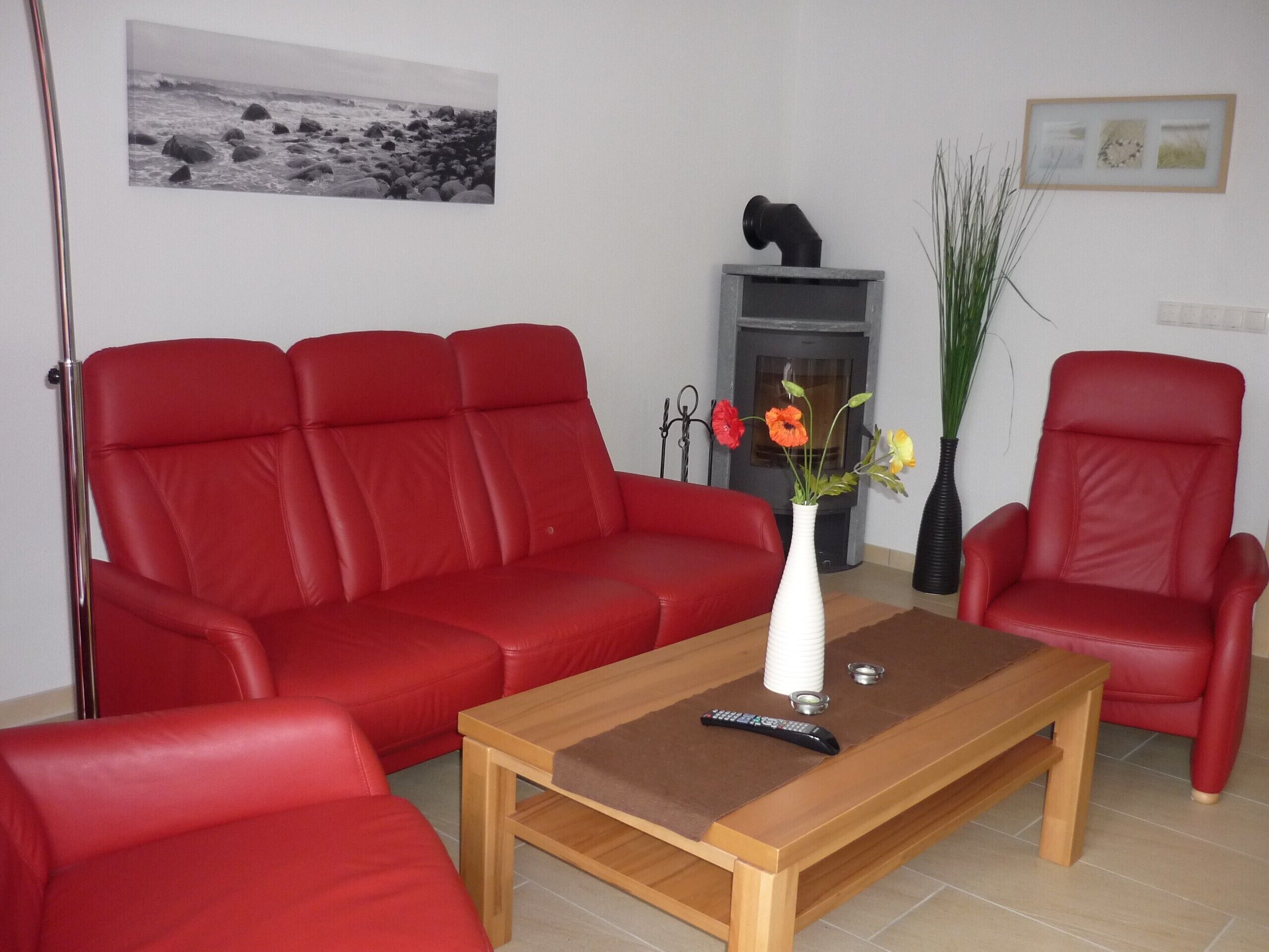 A living room with a red sofa, a wooden coffee table, and a red armchair. There is a fireplace with a black sculpture on top, a vase with flowers, and a framed picture on the wall.