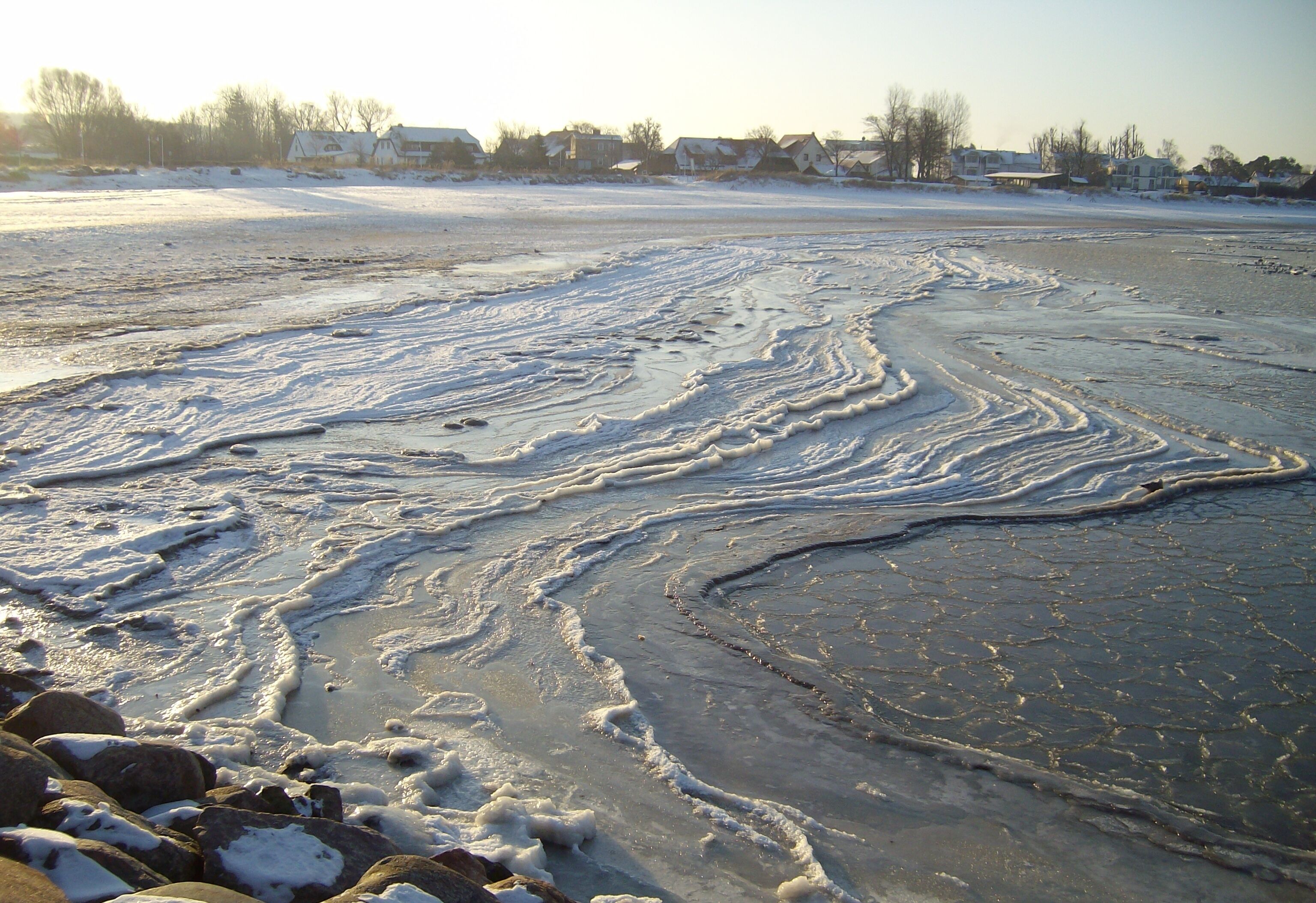 A frozen lake with visible ice patterns and surrounding residential houses.