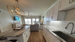 A modern kitchen with a marble countertop, stainless steel sink, and white cabinetry.