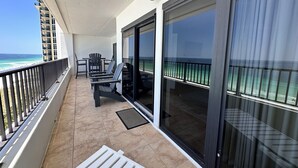 A balcony with a view of the ocean, a table with chairs, and a sliding glass door.
