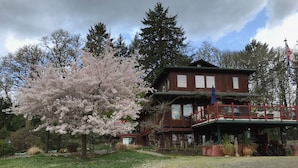 Un bâtiment en bois à deux étages, doté d’un balcon, entouré d’arbres et bordé d’une allée en gravier.