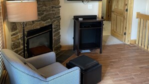 Un soggiorno con camino in pietra, una TV a schermo piatto montata sopra, un divano, un tavolino da caffè e una porta in legno.