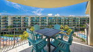 A balcony with a table and chairs, overlooking a swimming pool and a hotel building with multiple balconies. - 3 BR 3 BA - Phoenix on the Bay Condo 1428 (Orange Beach)