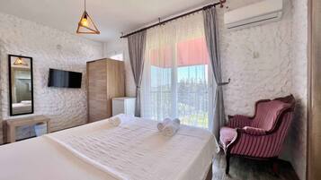 A bedroom with a bed, a chair, a TV, and a window with curtains.