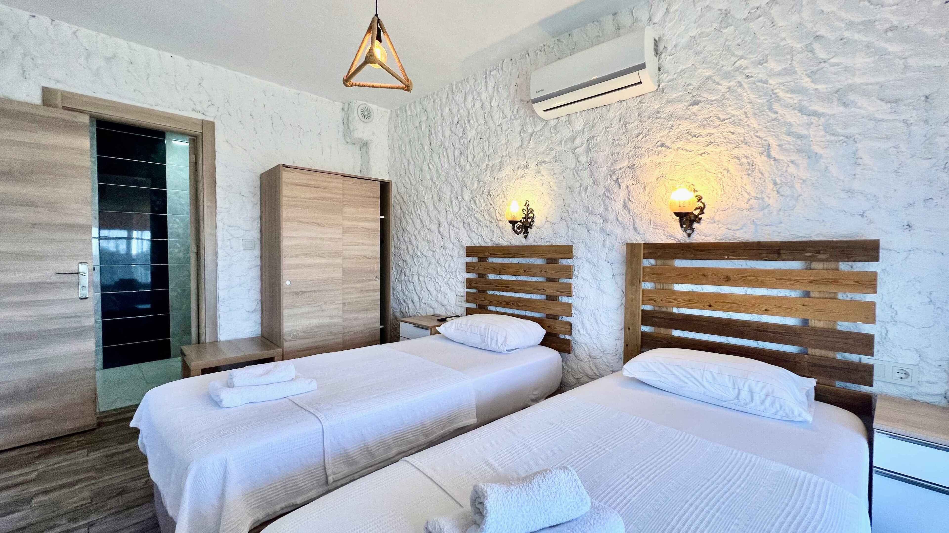 A bedroom with two beds, wooden headboards, a hanging light fixture, an air conditioning unit, and a wardrobe.