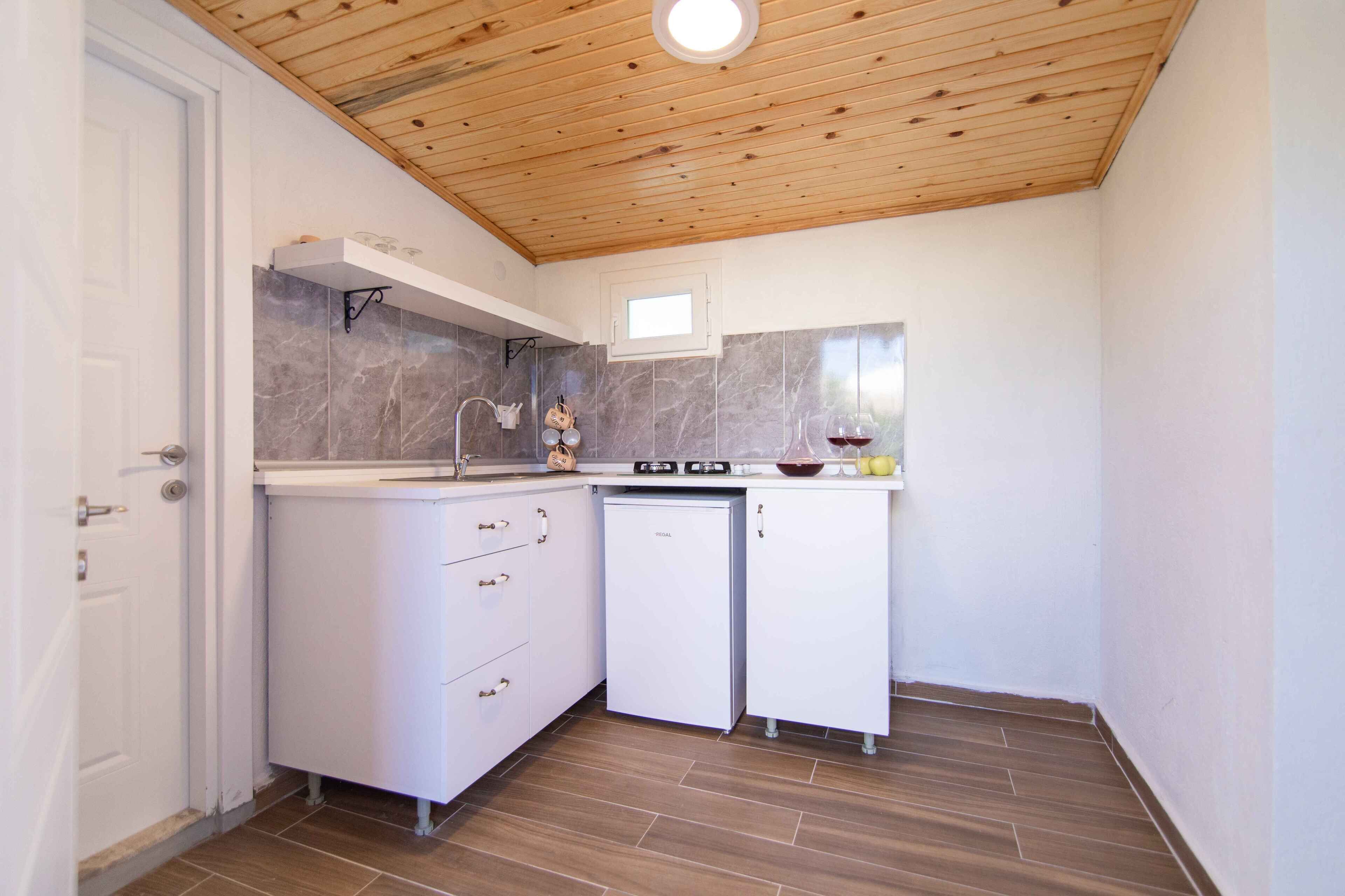A compact kitchen with white cabinets, a marble backsplash, and a wooden ceiling.