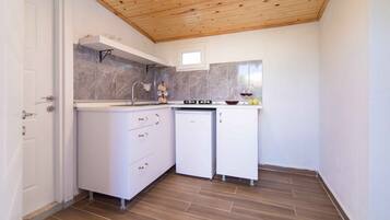 A compact kitchen with white cabinets, a marble backsplash, and a wooden ceiling.