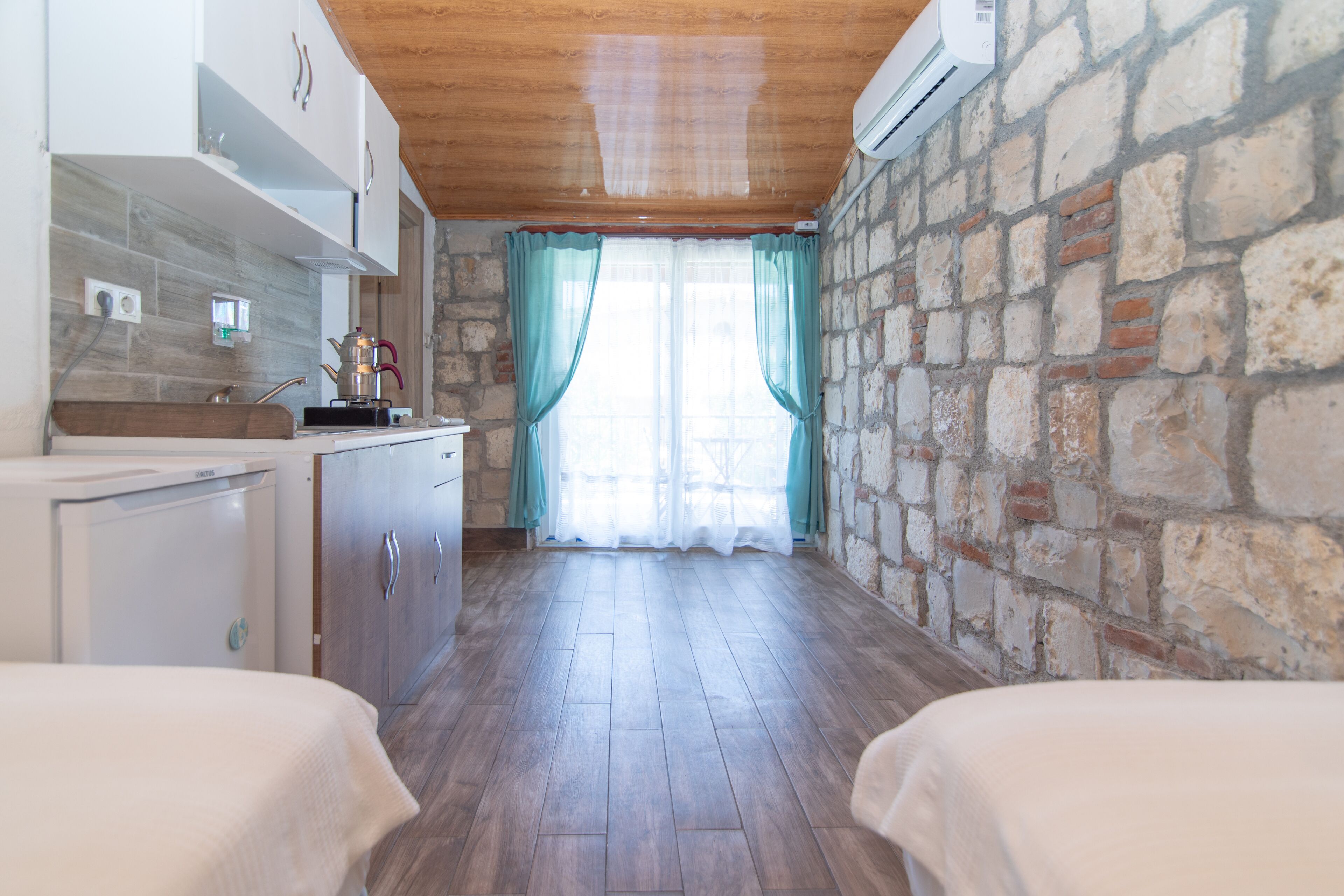 Une cuisine avec un mur en pierre, un plafond en bois et une fenêtre avec des rideaux.