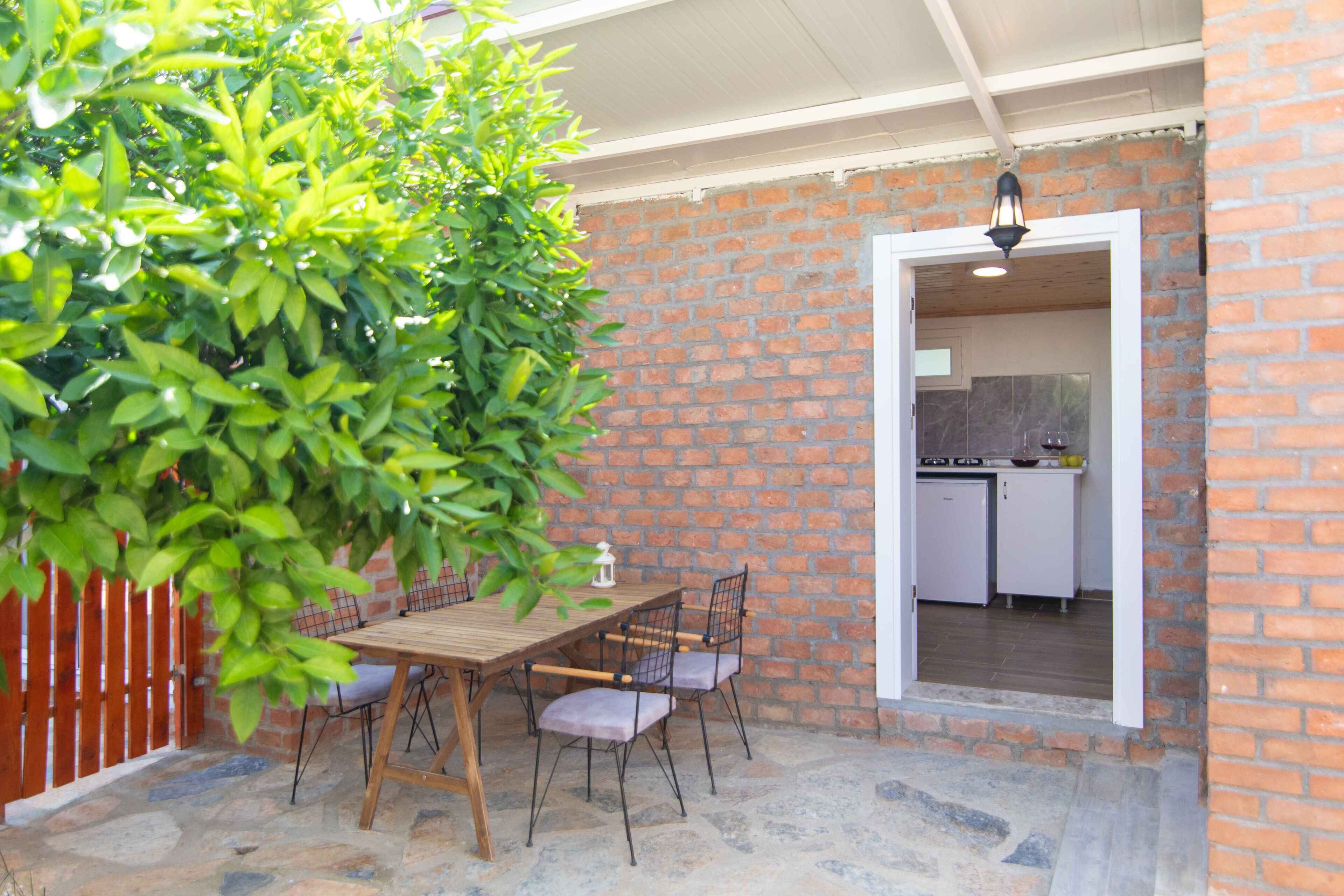 An outdoor patio with a wooden table and chairs, a brick wall, and a view into a kitchen area.