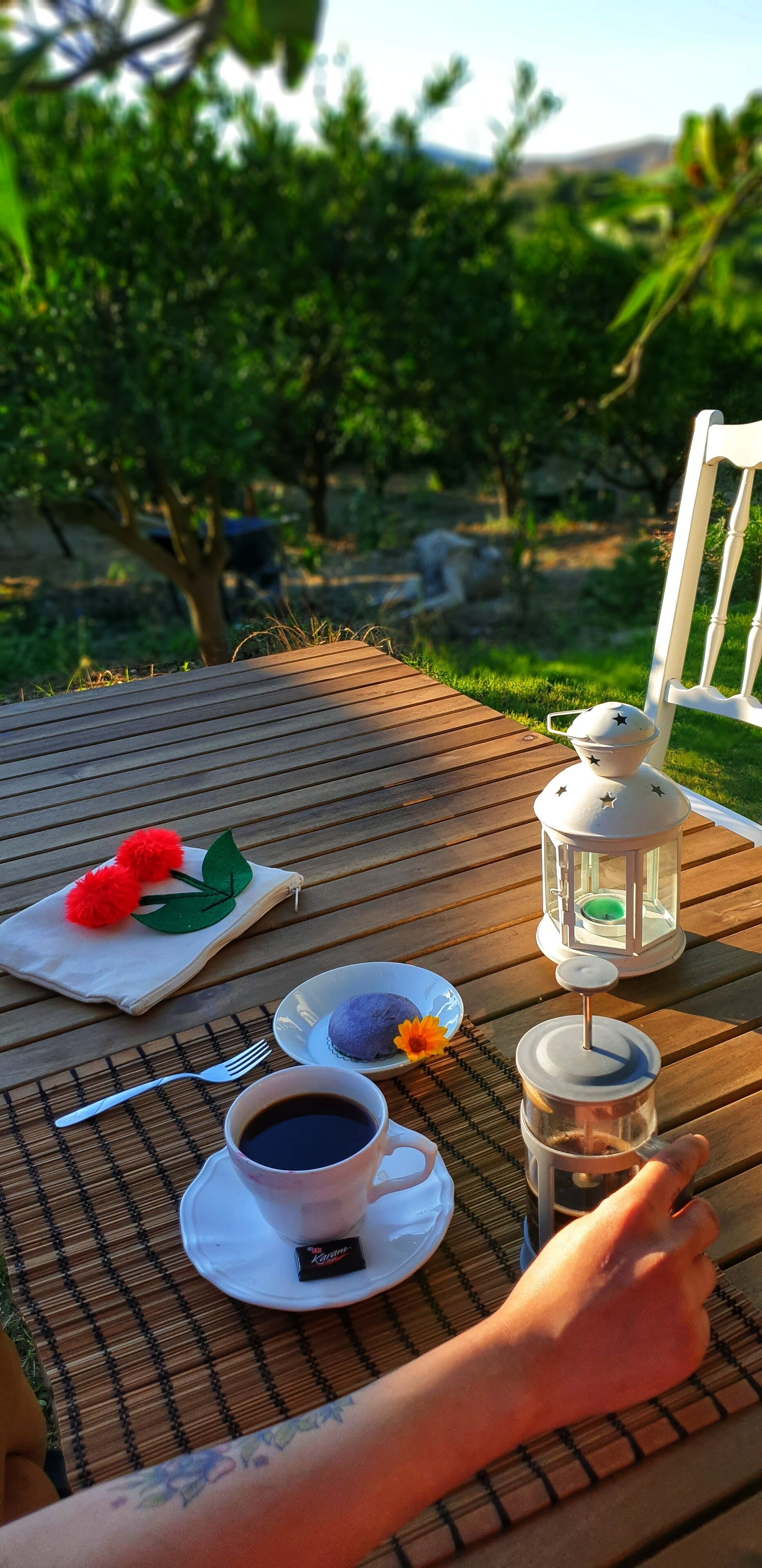 Cubierta de madera con una mesa lista para una comida, que incluye una taza de café, un plato con comida, un farol y una servilleta decorada.