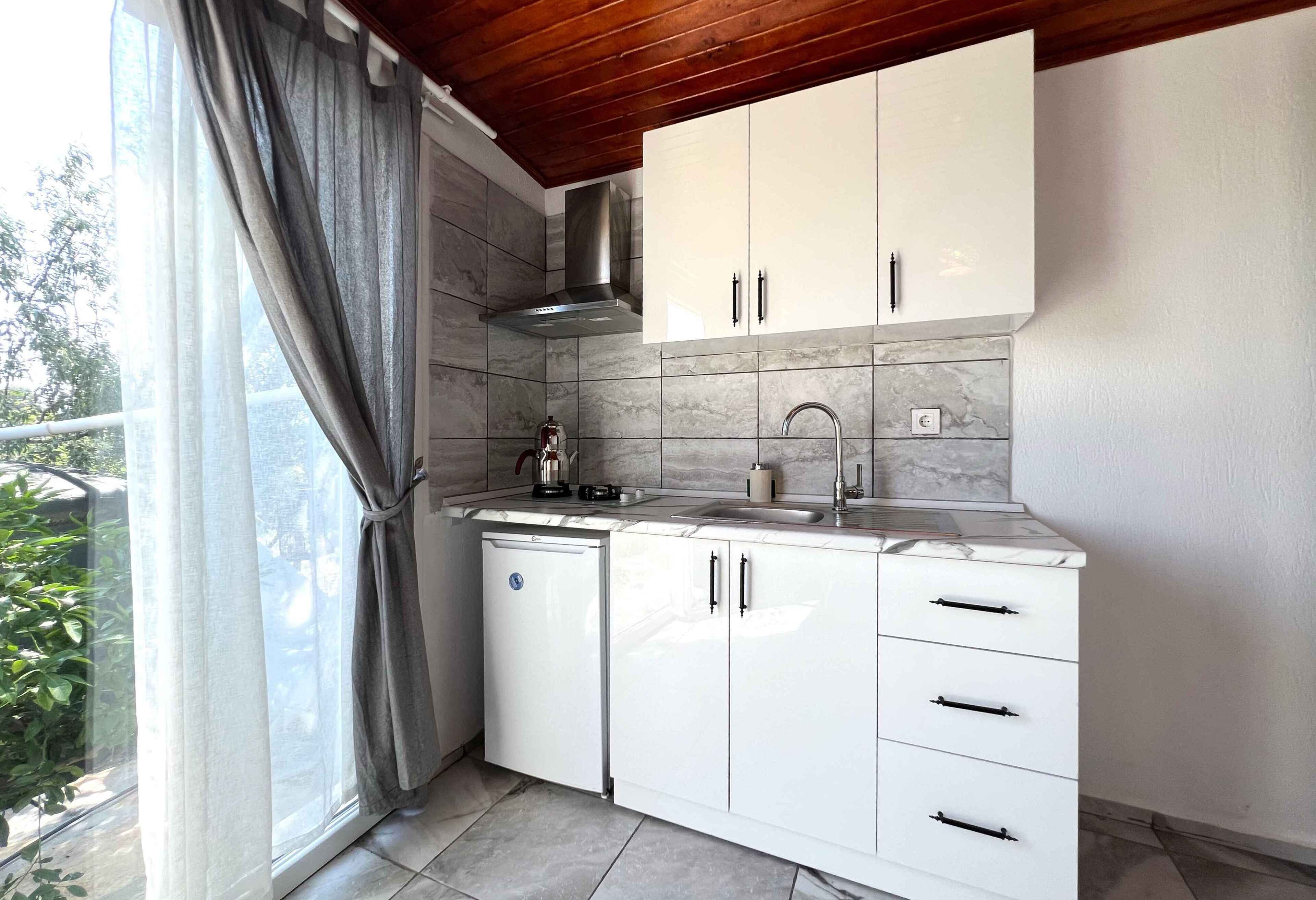 A modern kitchen with white cabinets, a stainless steel range hood, and a window with grey curtains.