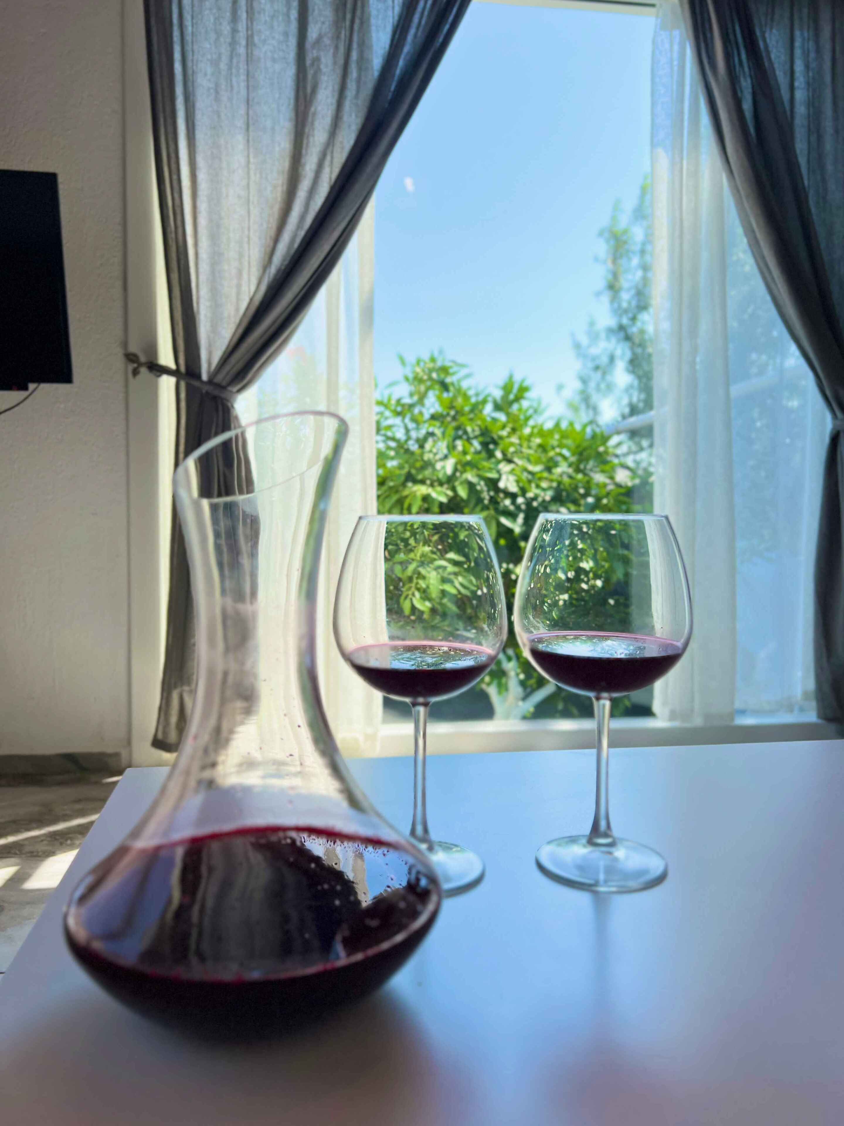 Ein Tisch mit einer Weinflasche und zwei Weingläsern an einem Fenster mit Vorhängen.