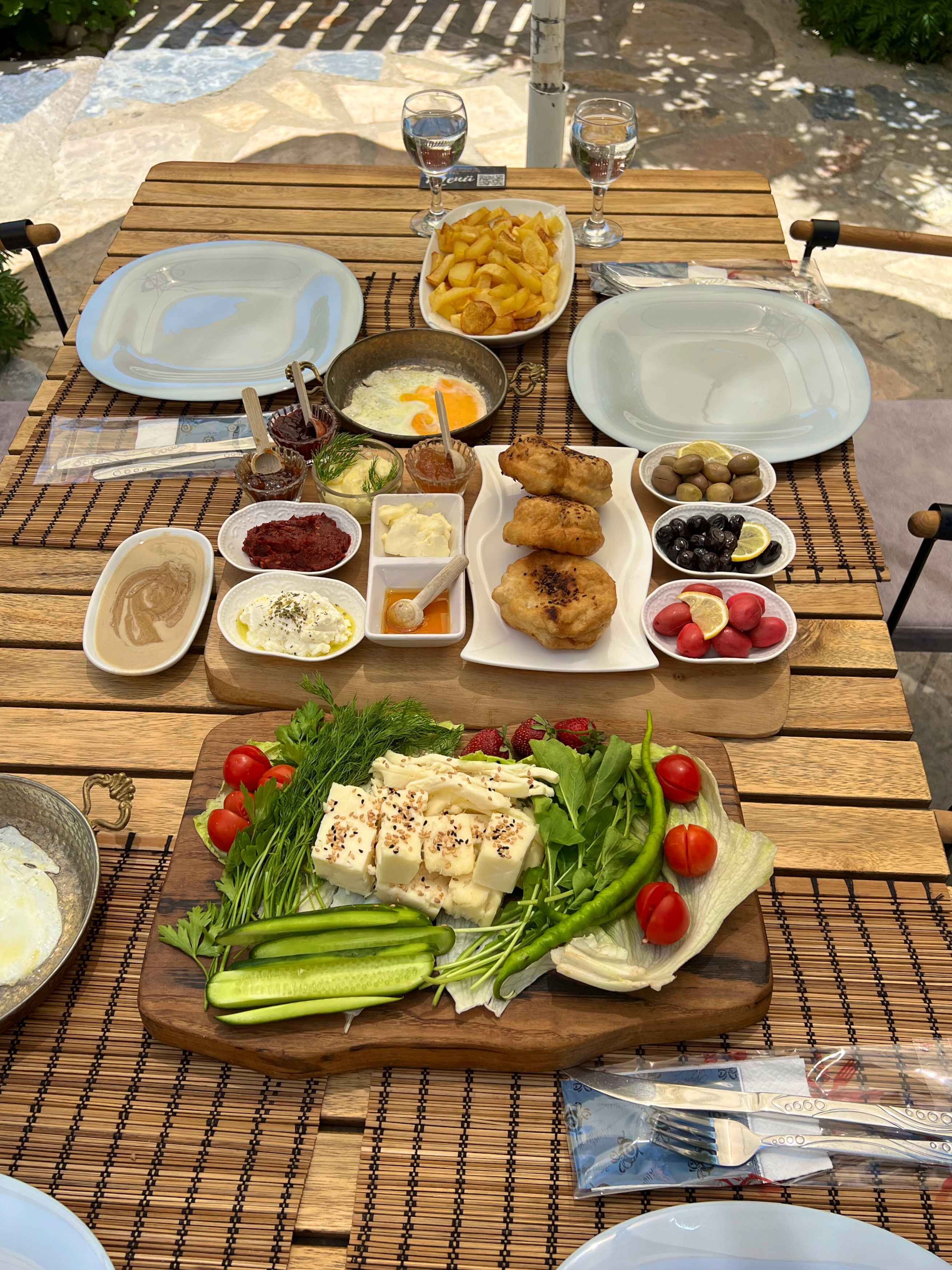 A wooden table set with various dishes including bread, olives, and a salad with tomatoes and cucumbers.