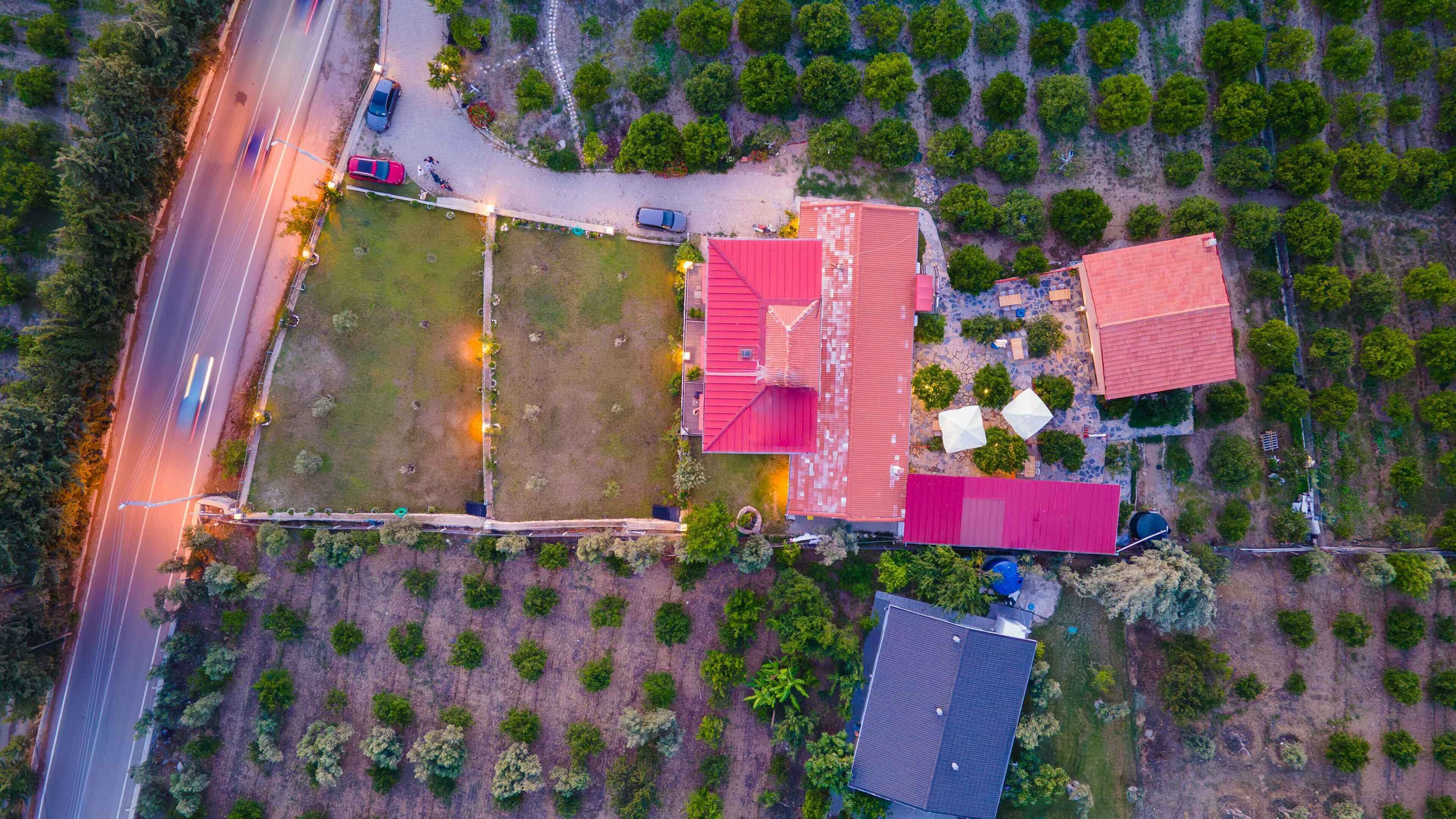 Vista aérea de una propiedad con un amplio campo abierto, un edificio de techo rojo y una estructura más pequeña de techo azul.