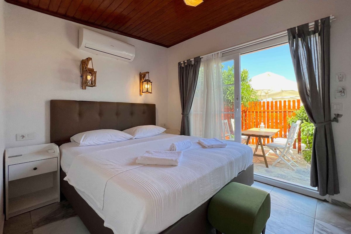 Quarto com cama grande, mesa de cabeceira, ar condicionado e vista para o pátio exterior.