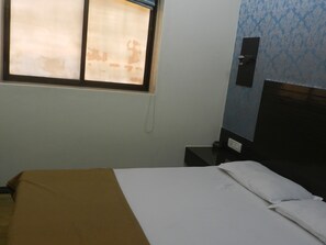 A room with a bed, a nightstand, a wall-mounted telephone, and a window with a curtain. - Hotel sweet home (Mumbai)