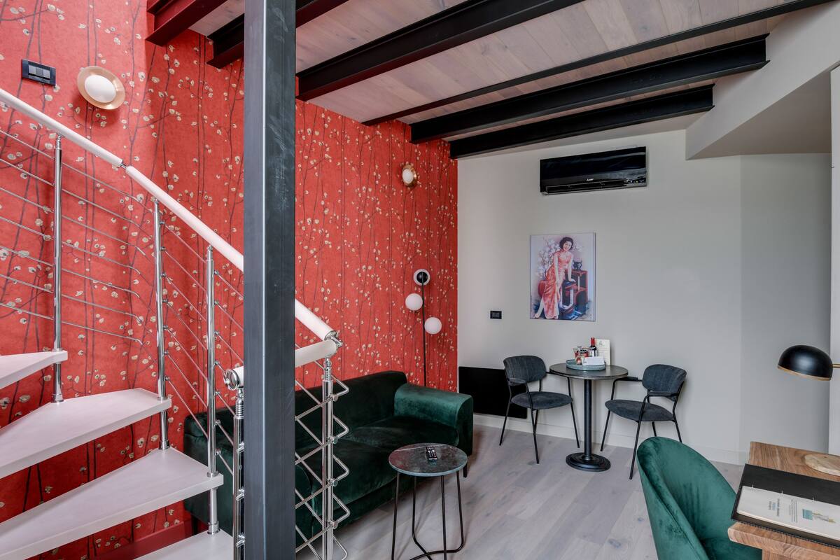 Un espace de vie moderne avec un papier peint à motifs floraux rouges, un canapé vert, une petite table ronde et un escalier doté de rampes en métal.