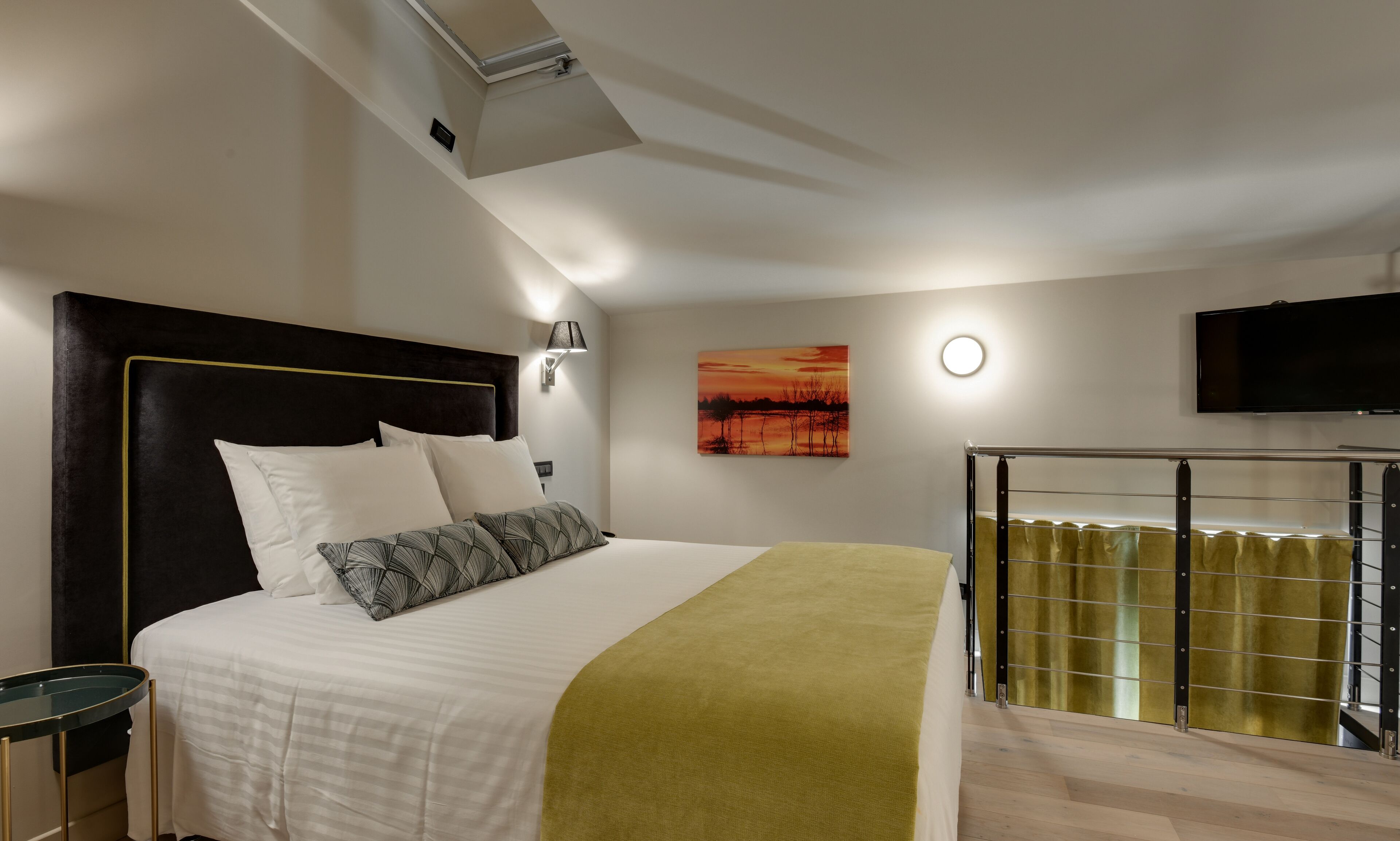 A modern hotel room with a large bed, a flat-screen TV mounted on the wall, and a ceiling fan.