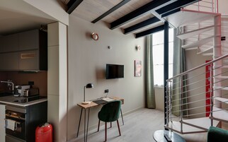 Una cocina moderna con horno empotrado, un cilindro de gas rojo y una zona de comedor con una silla verde y una mesa de madera.