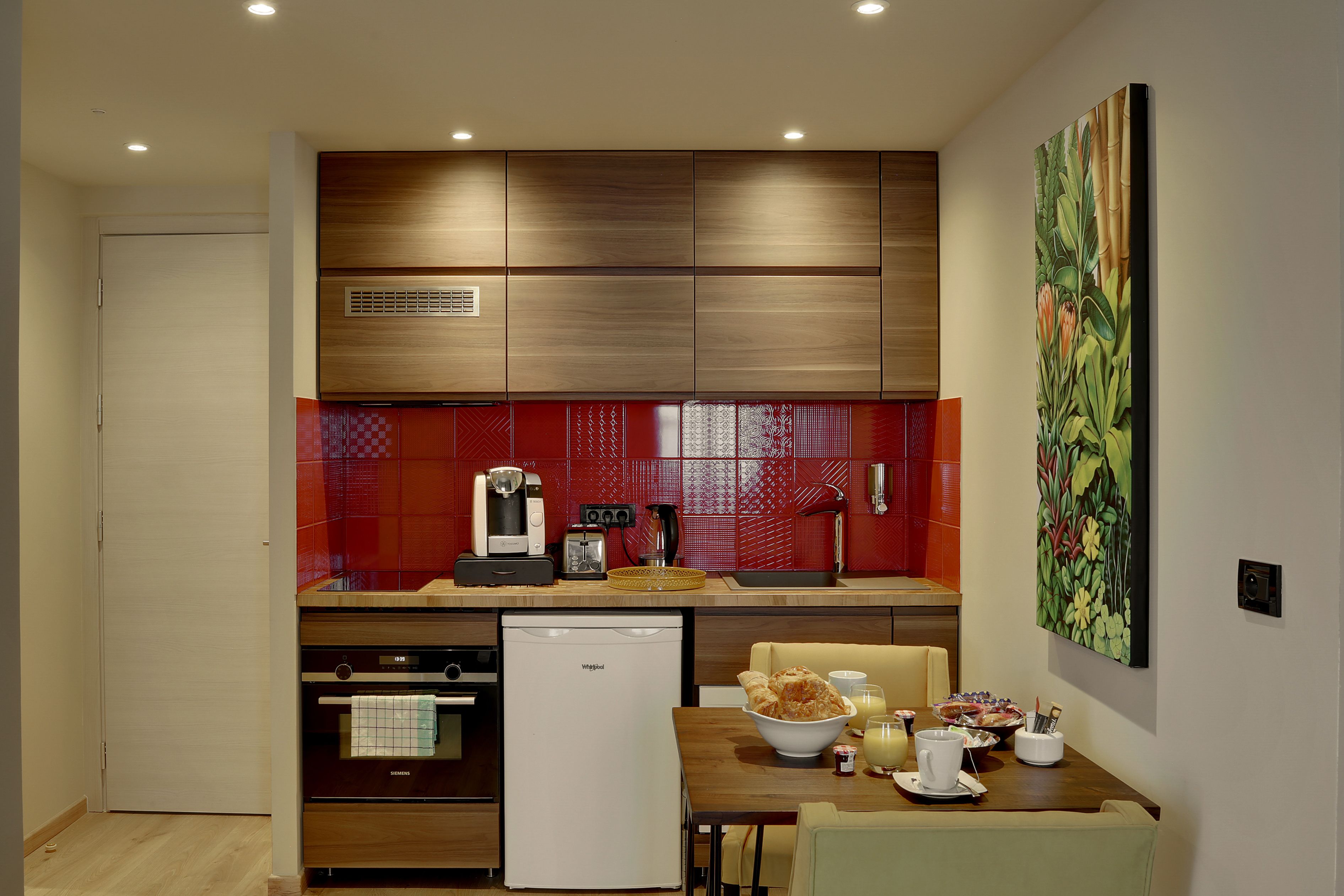 Una cocina compacta con refrigerador, cafetera y comedor con mesa y sillas.