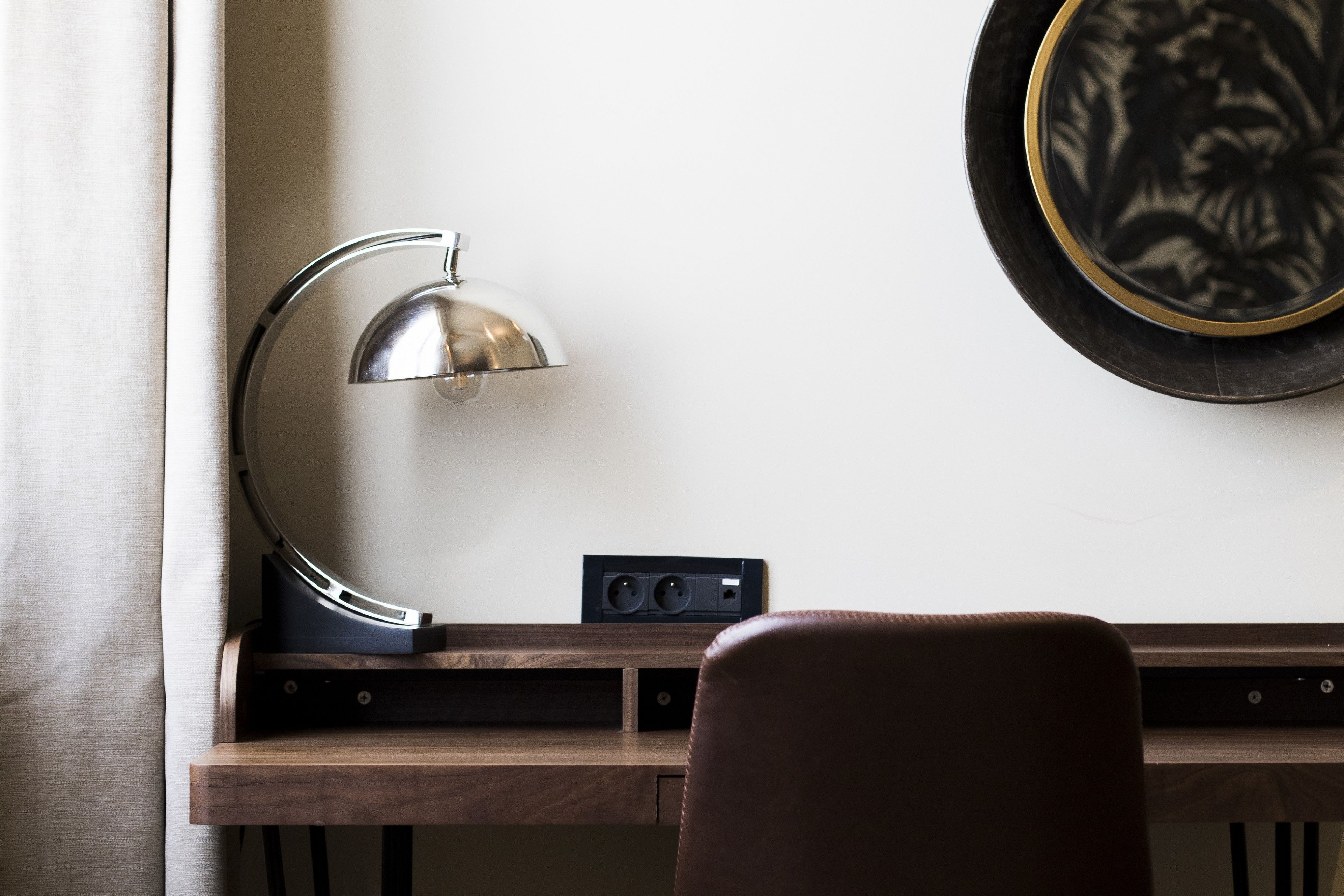 Uma mesa com luminária, régua de tomada e um quadro na parede.