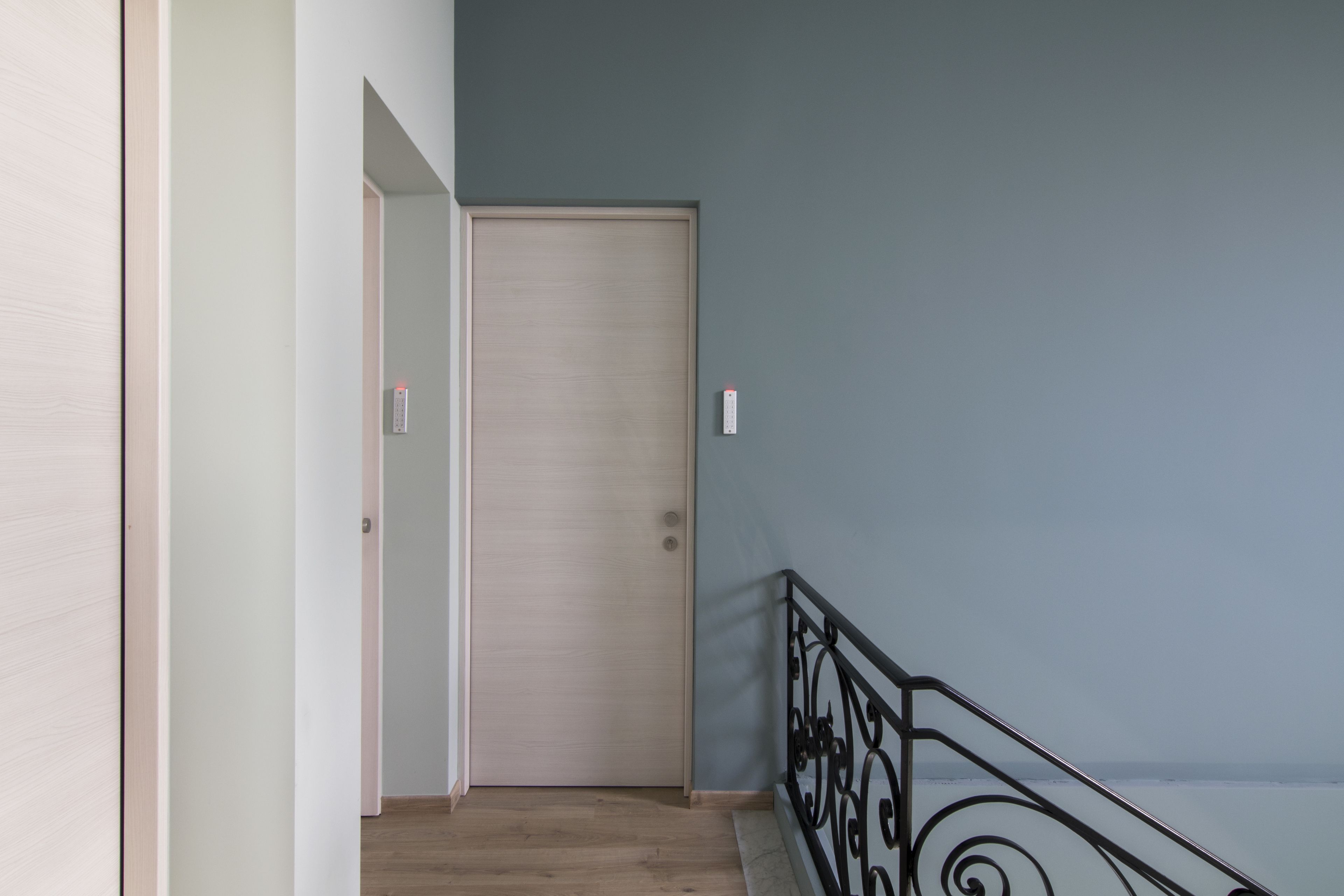 Um corredor com piso de madeira, uma porta fechada e um guarda-corpo de metal preto.