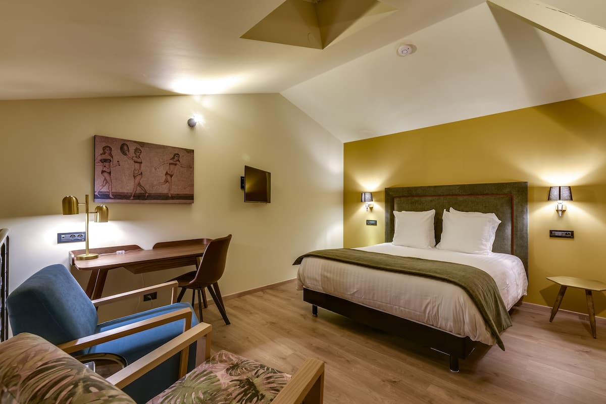 Une chambre d’hôtel avec un lit, un bureau et une chaise, un tableau au mur et une petite table.
