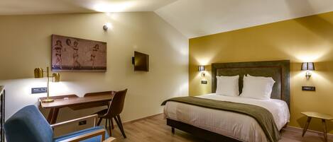 Habitación de hotel con cama, escritorio, silla, un cuadro en la pared y una mesita.