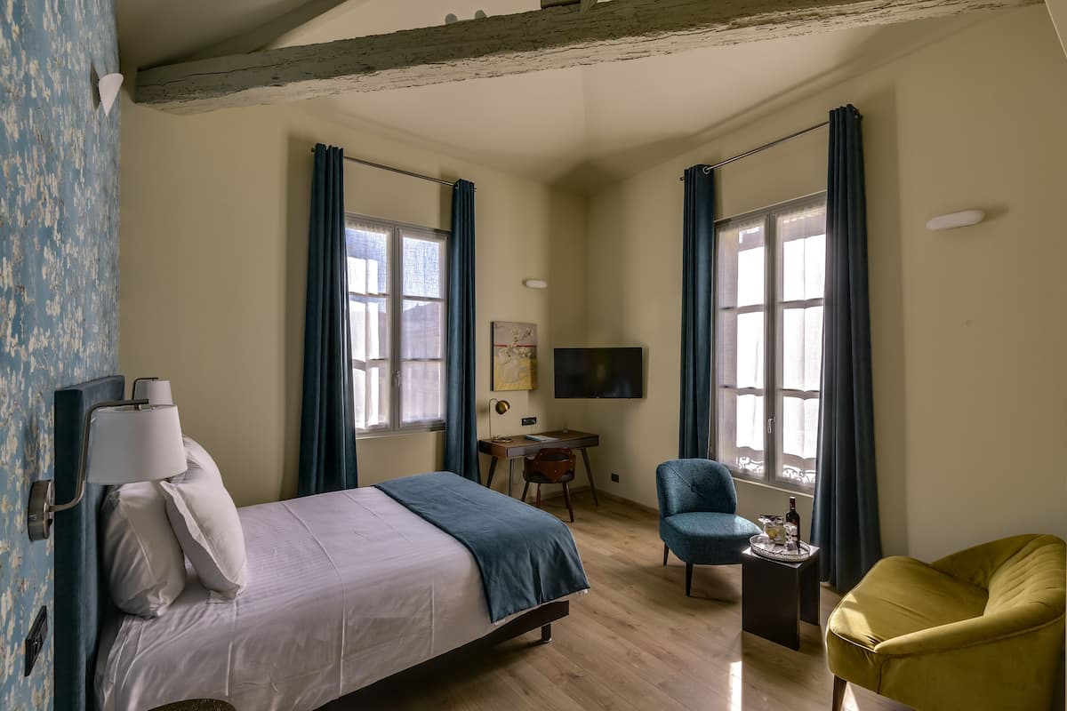 Une chambre à coucher avec un lit, un bureau, une chaise, un téléviseur et une fenêtre avec des rideaux.