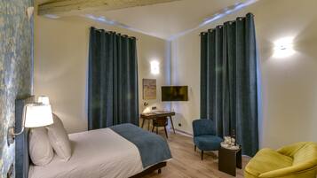 A hotel room with a bed, a desk, a chair, a TV, and a small table with a bottle and glasses.