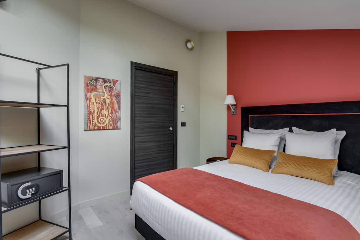 Une chambre d’hôtel moderne, équipée d’un lit, d’une table de chevet, d’une lampe fixée au mur, d’un tableau et d’une porte.