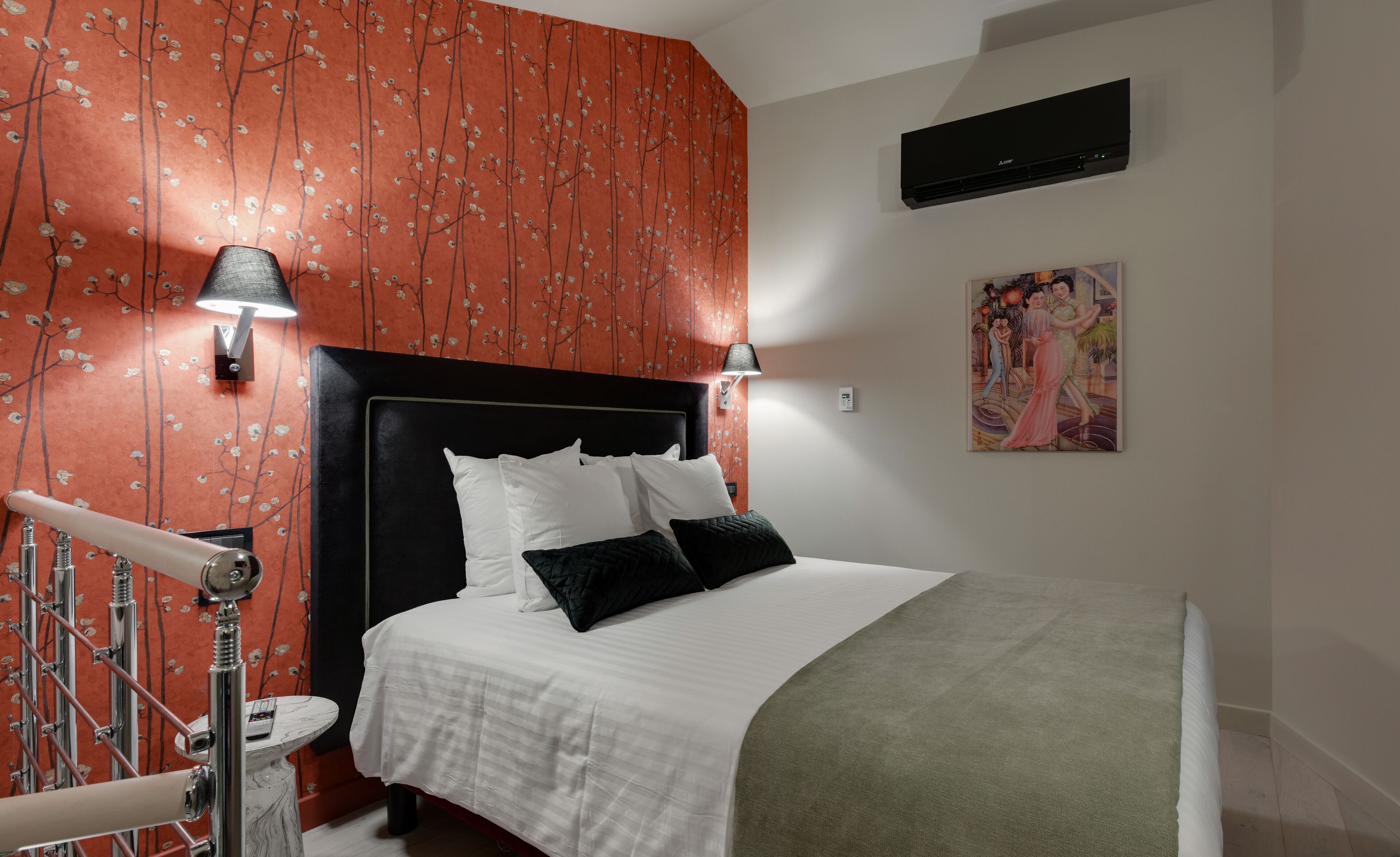 Habitación de hotel con cama, dos lámparas de pared, un cuadro y aire acondicionado en el techo.