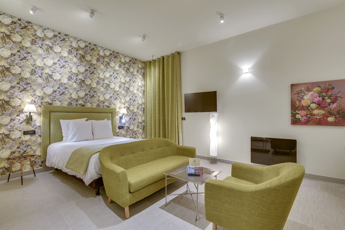 Une chambre d’hôtel avec un lit, un canapé vert, une petite table, un téléviseur et un tableau floral accroché au mur.