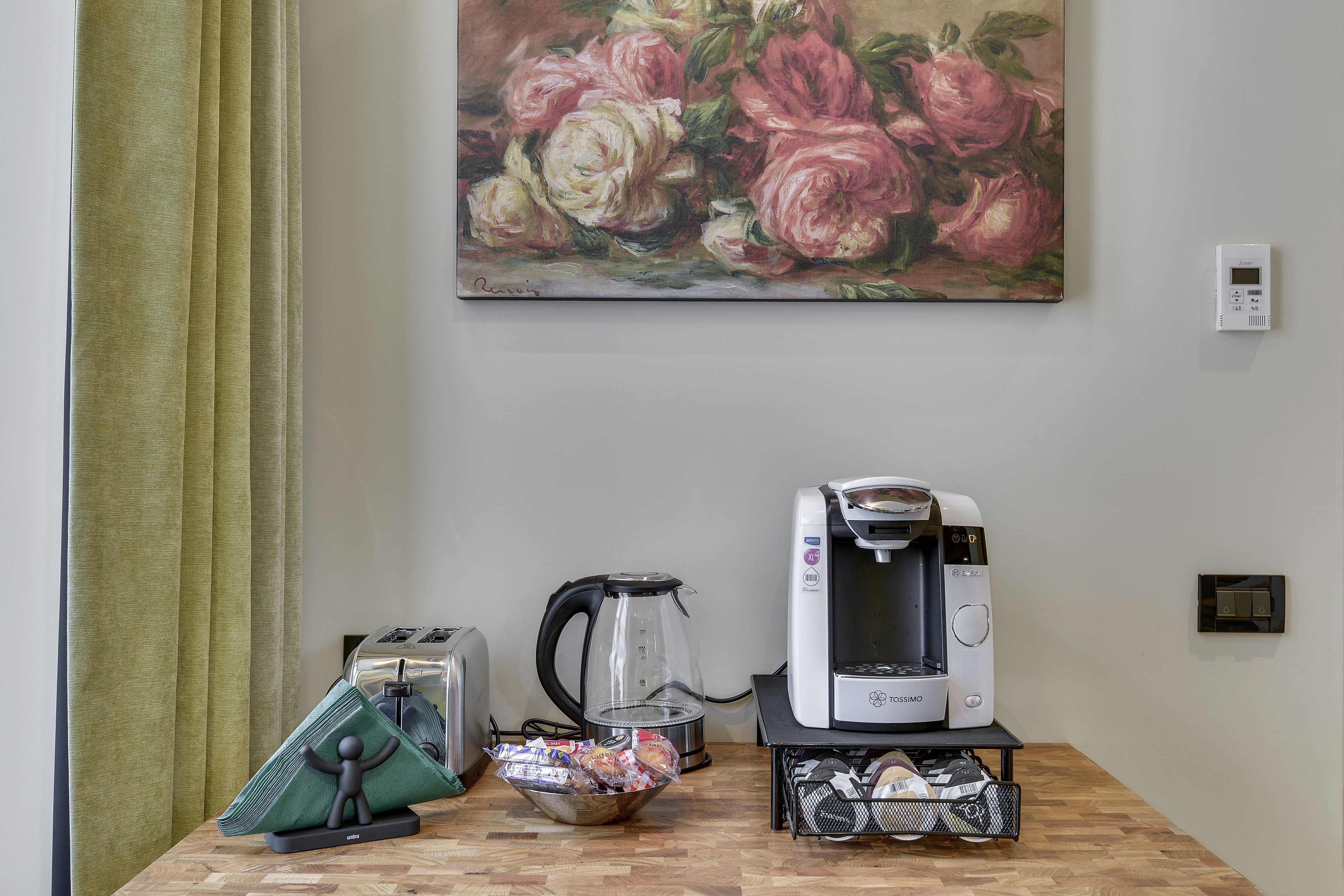 Et tekøkken med kaffemaskine, brødrister, elkedel og en skål med snacks på et træbord.