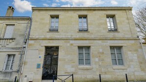 Un bâtiment à deux étages doté d’une façade en pierre, d’une entrée centrale avec une porte décorative et d’un petit balcon au deuxième étage.