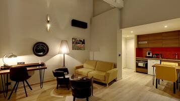 Ein modernes Wohnzimmer mit einer Couch, einem Schreibtisch und einer Lampe. Es gibt eine Küchenzeile mit roten Fliesen und Holzschränken.