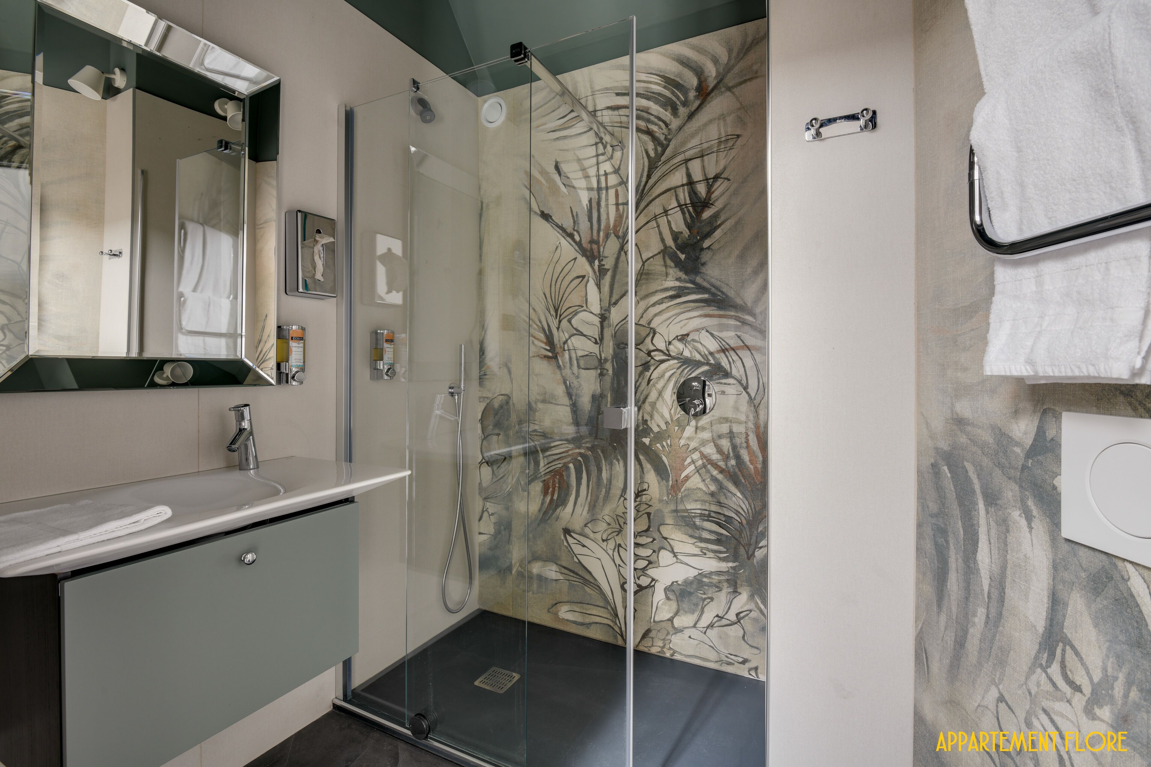 A modern bathroom with a glass shower enclosure, a sink with a mirror, and a towel rack.