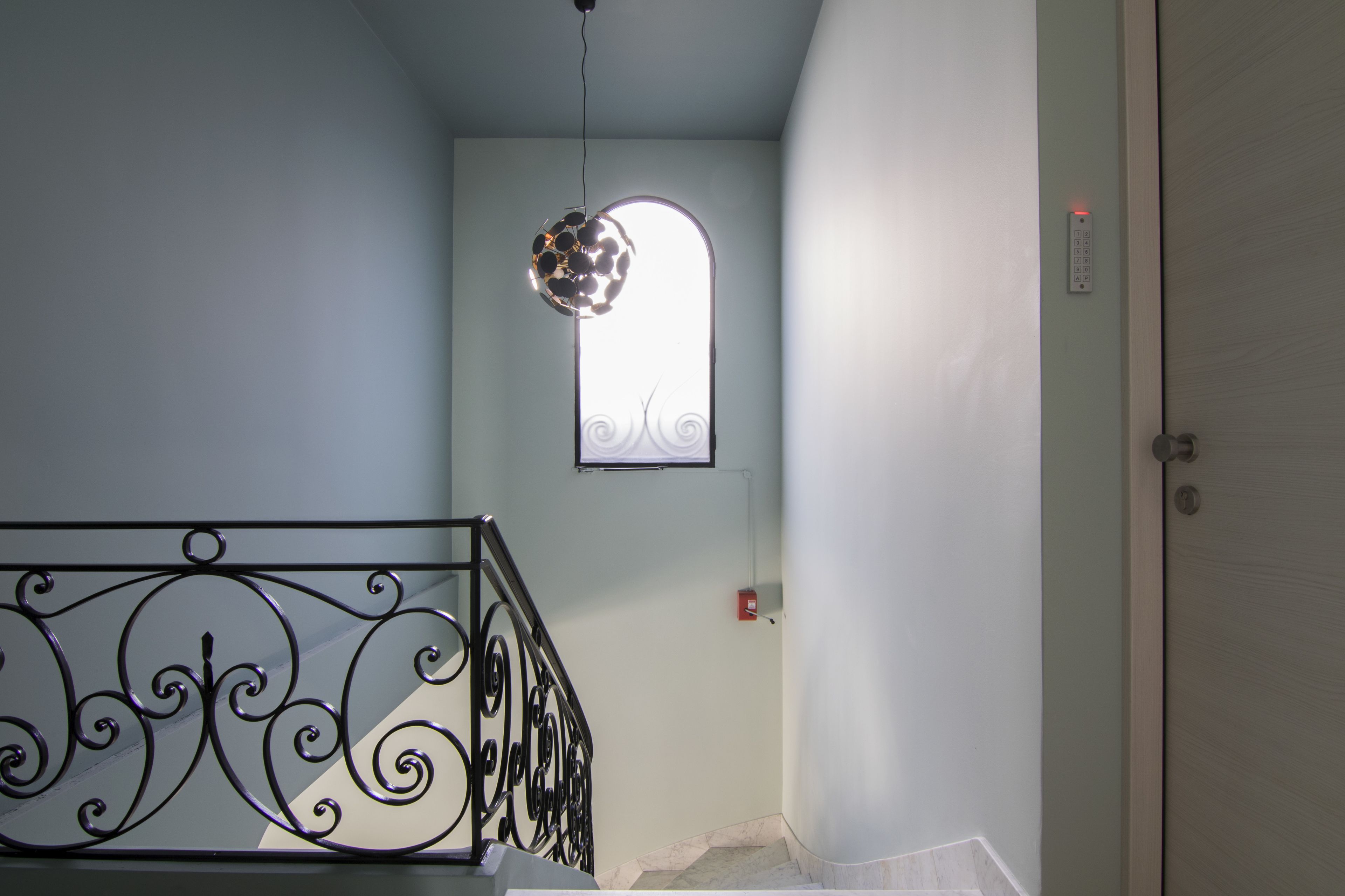 A staircase with a decorative metal railing, a small window with a decorative design, and a door with a lock.