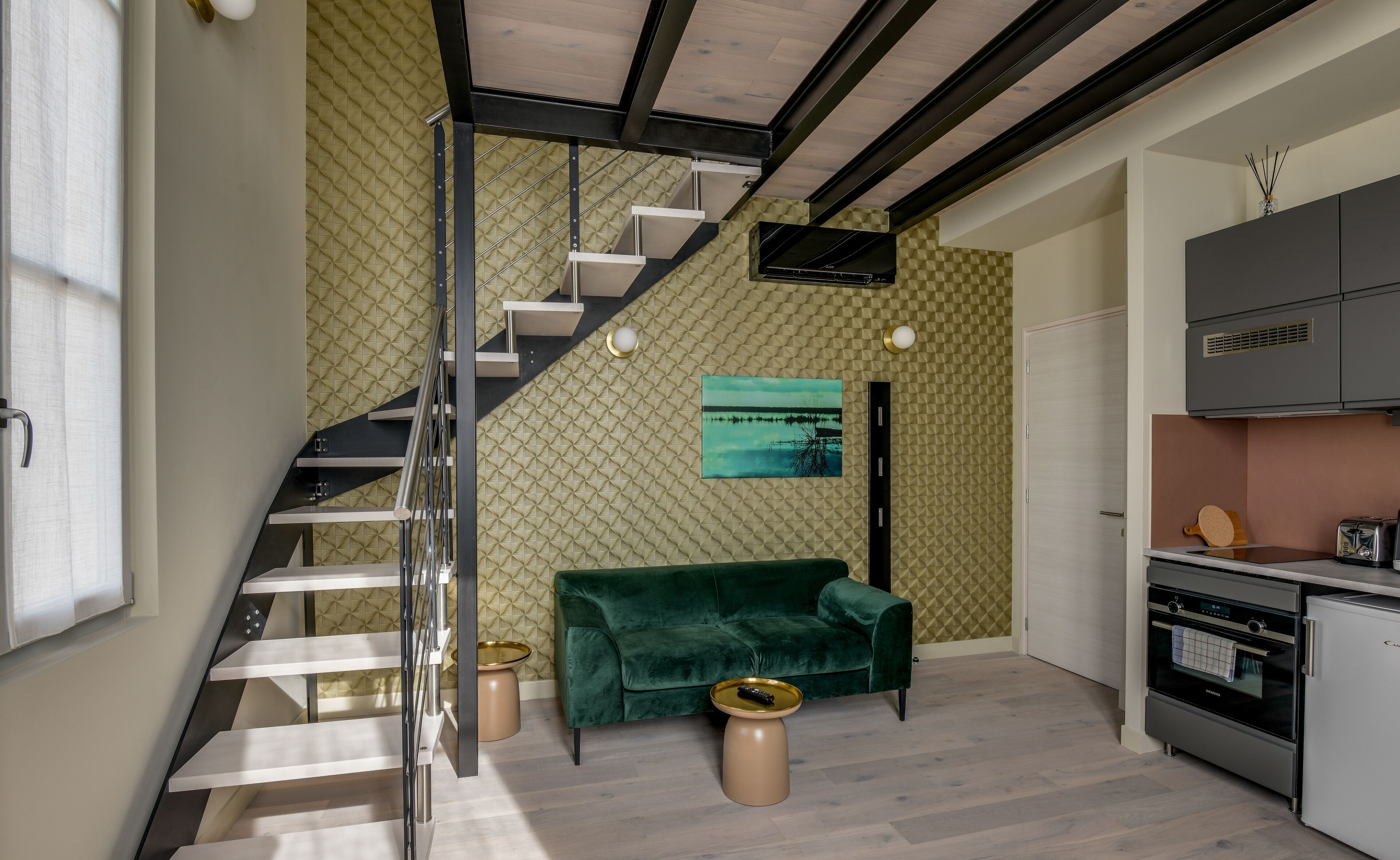 Una cocina moderna con horno empotrado y refrigerador, un sofá de terciopelo verde y una escalera con barandilla de metal.