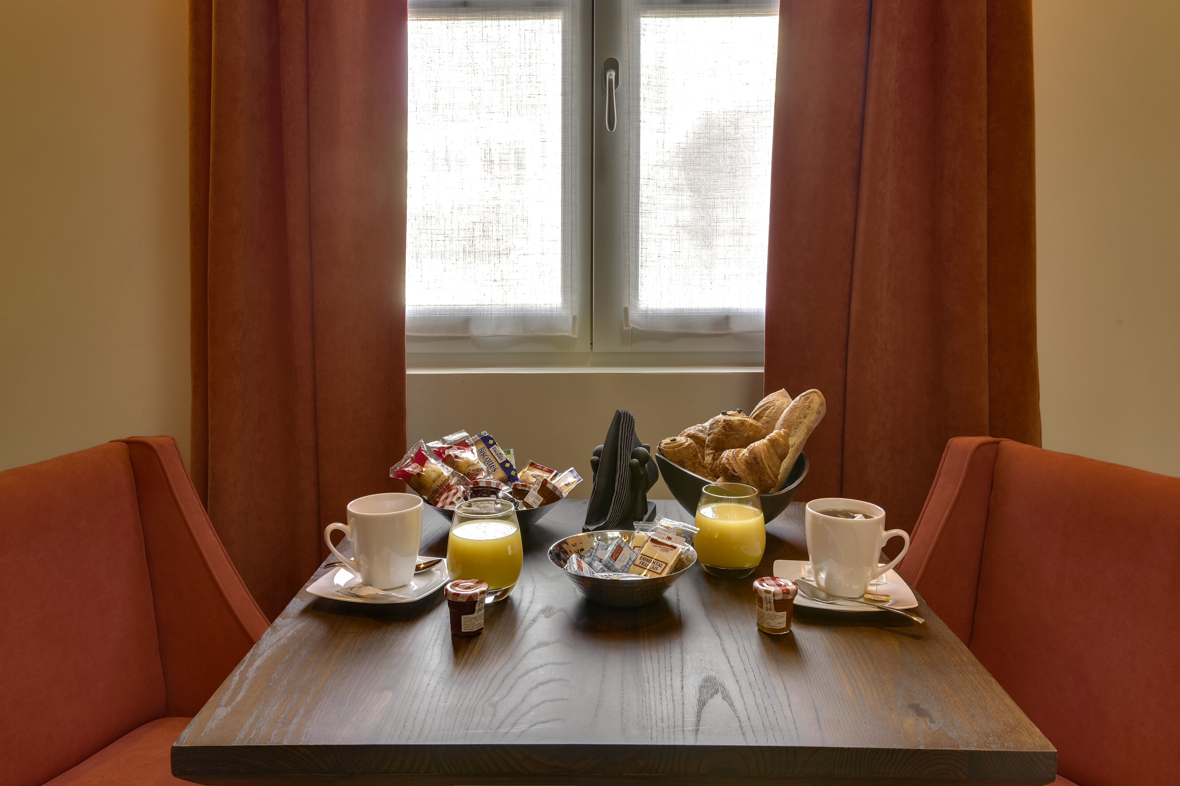 Une table de petit-déjeuner avec des croissants, du café, du jus de fruits et des viennoiseries.
