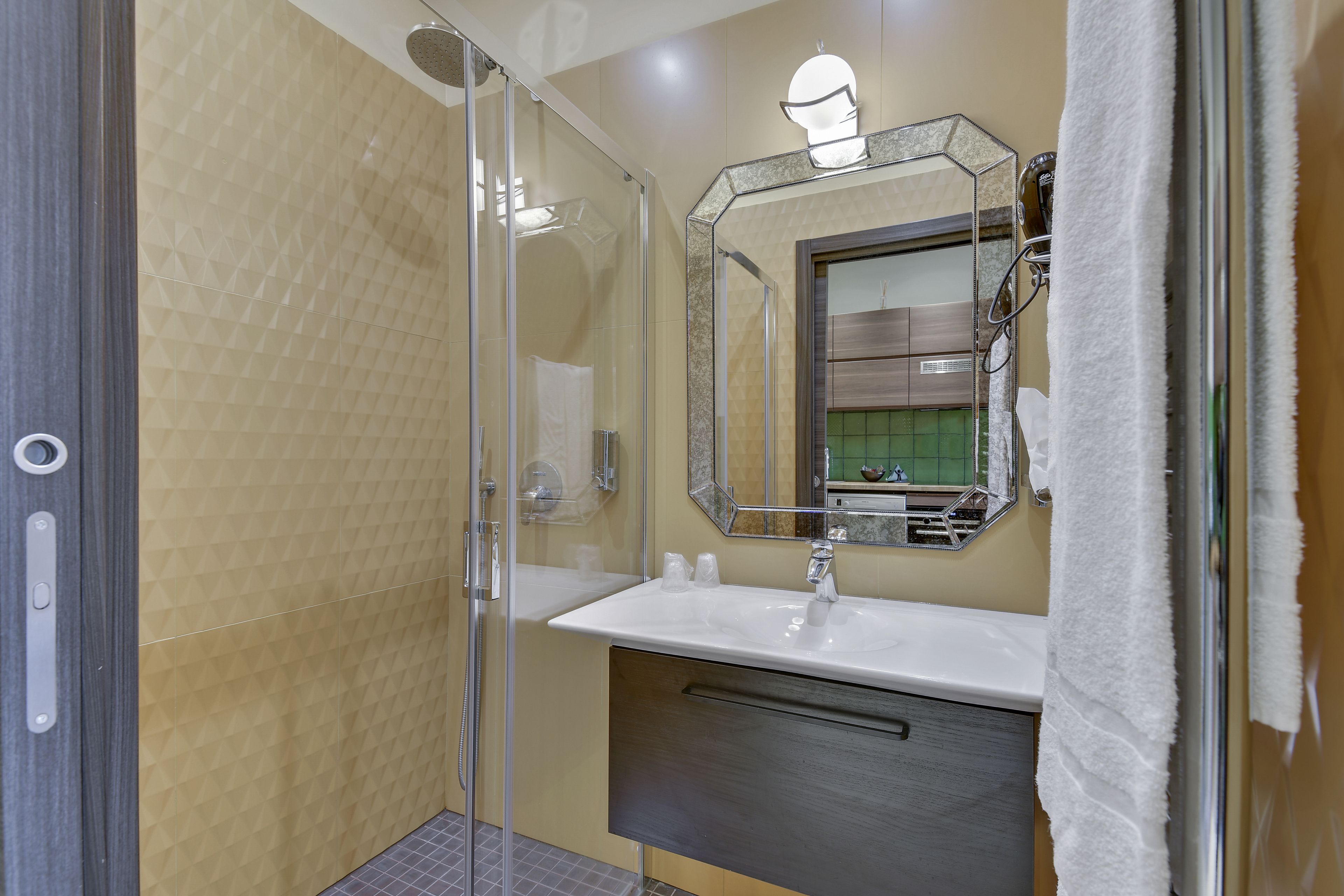 Een moderne badkamer met een glazen douchecabine, een witte wastafel en een grote spiegel.