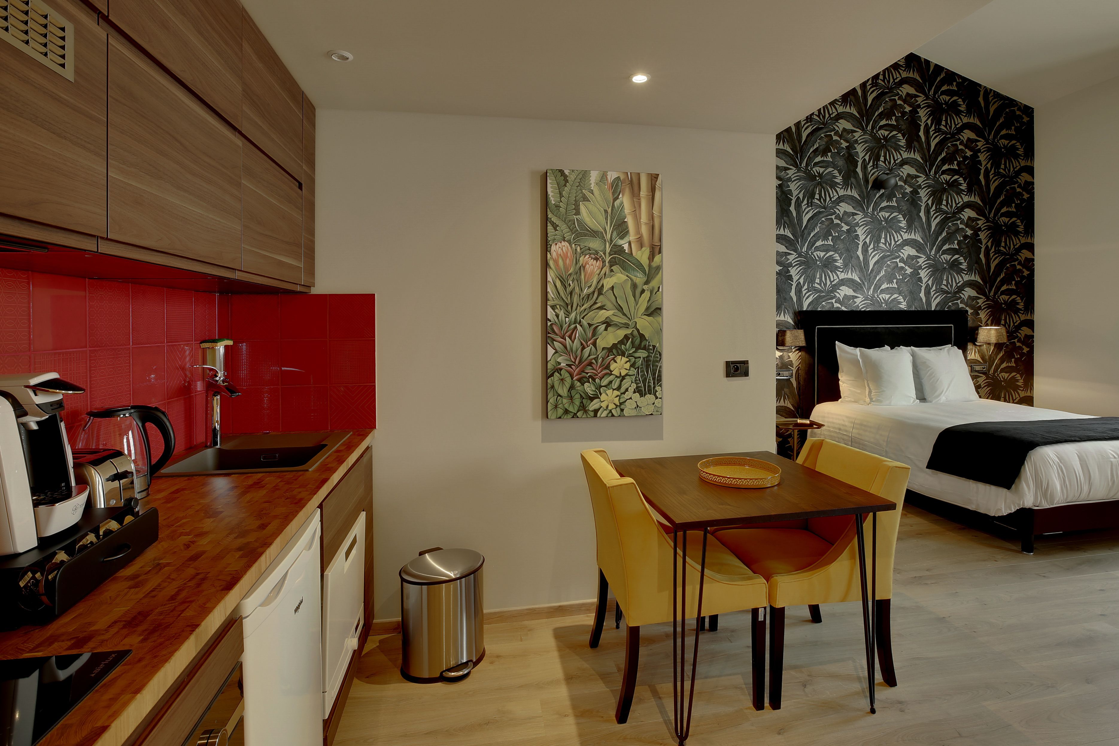 Een compacte hotelkamer met kitchenette, een zithoek en een bed met behangpapier met een groot bloemenpatroon.