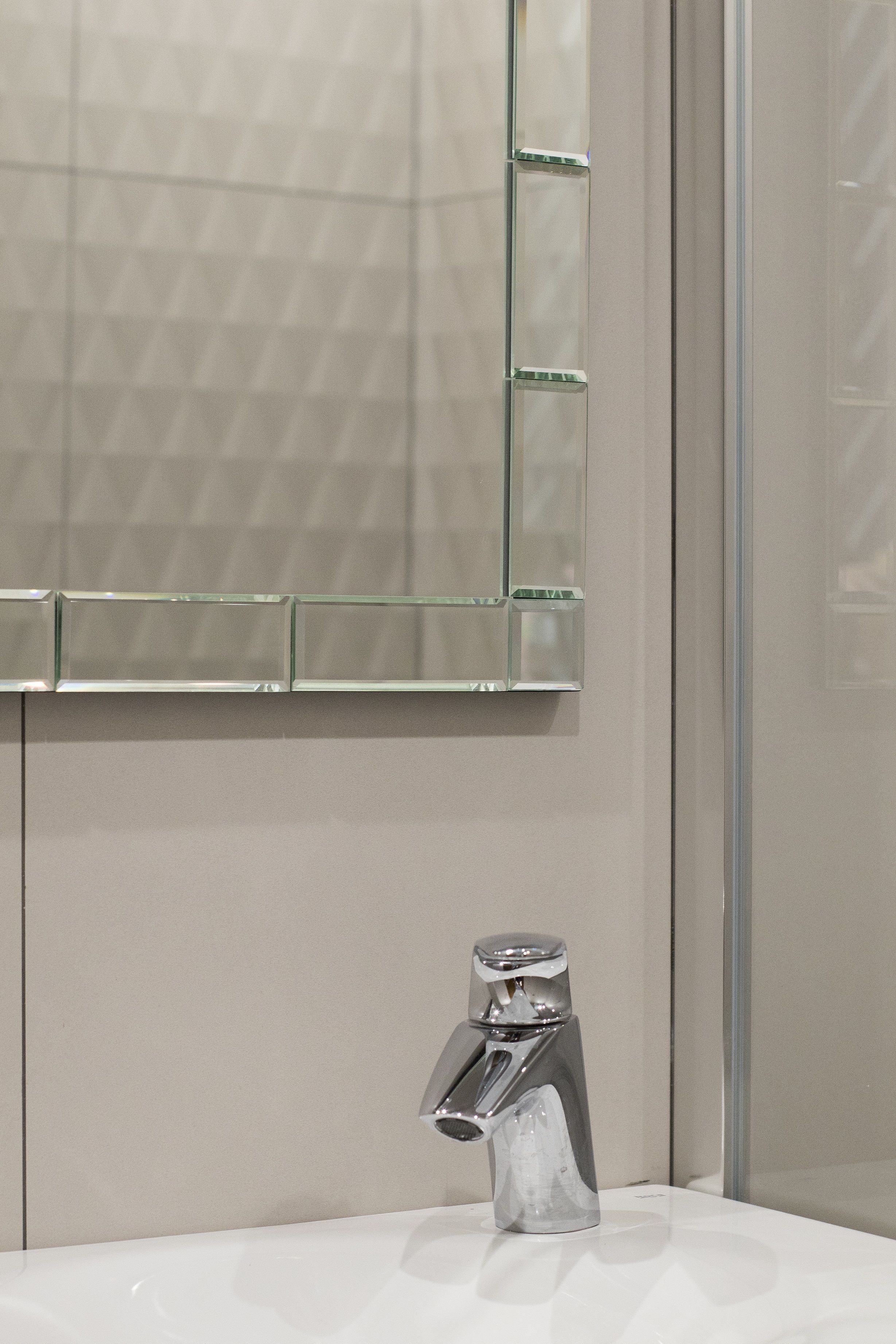 A bathroom with a modern sink, a glass shower enclosure, and a mirror with a geometric pattern.
